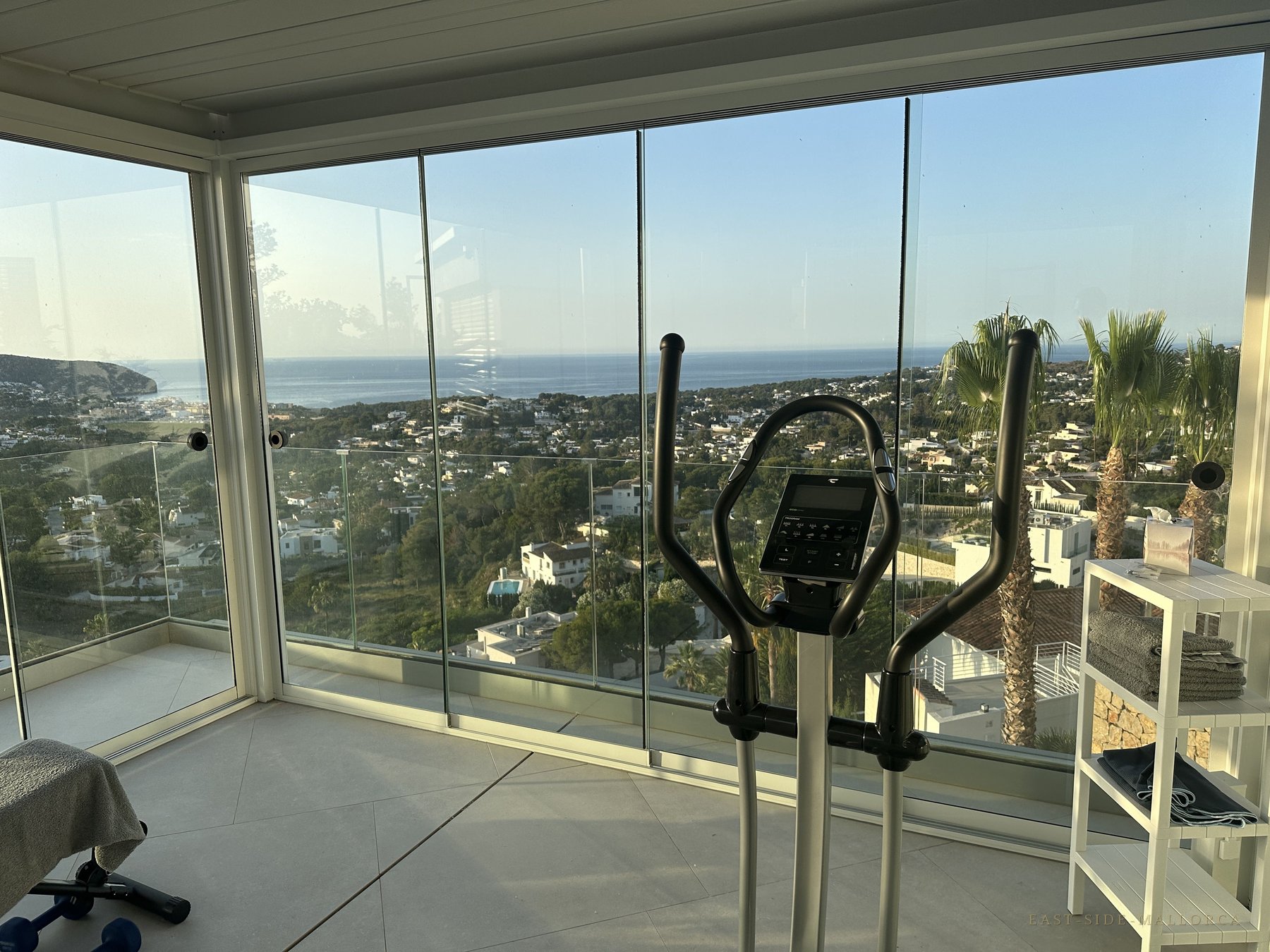 Verglaster Fitnessraum mit Crosstrainer und Panoramablick aufs Meer